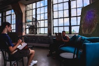 two people sitting in a room with large windows
